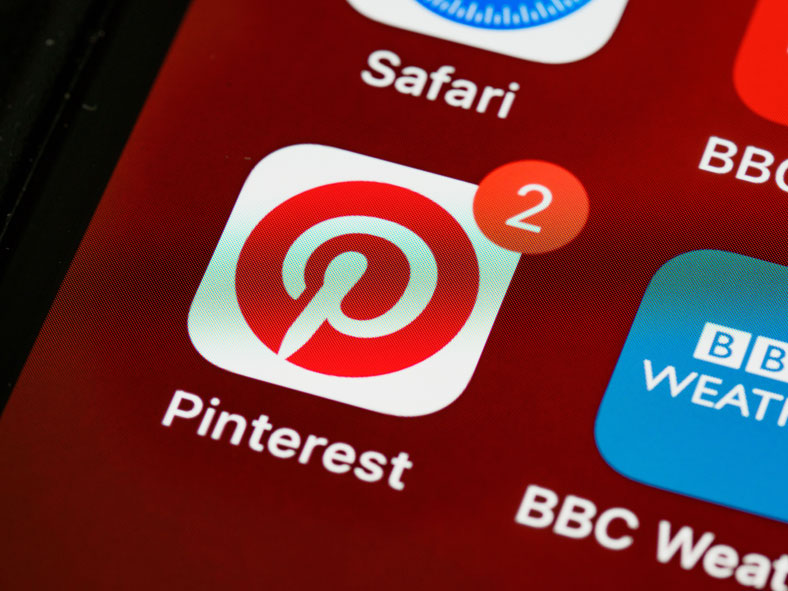 Gros plan sur l'écran d'un smartphone affichant l'icône de l'application Pinterest avec une pastille de notification rouge indiquant le chiffre 2.